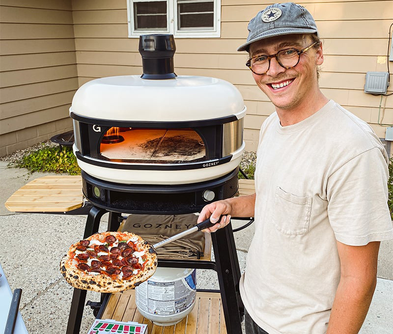 gozney pizza oven man holding pepperoni pizza with pizza peel smiling