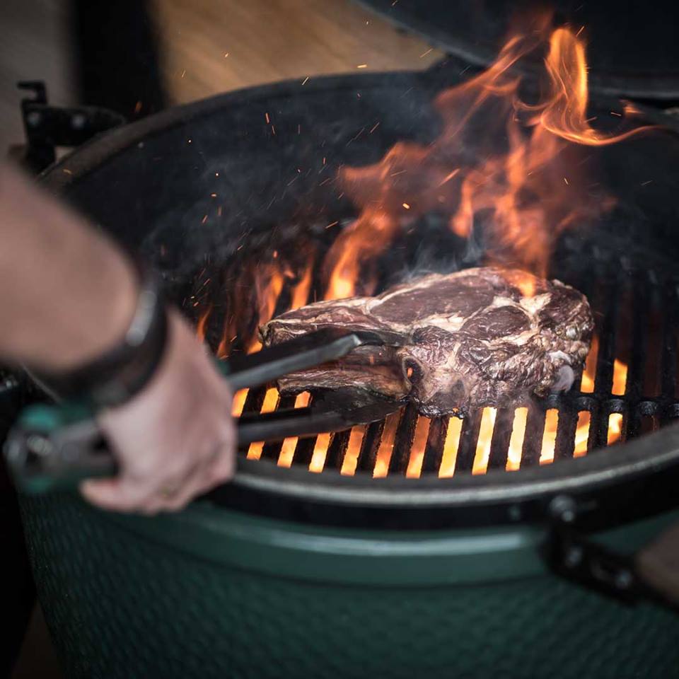 big green egg with steak and flames coming out
